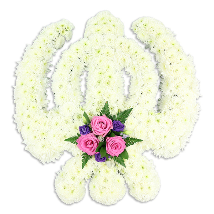 A beautifully composed photograph captures a large Sikh Khanda funeral tribute crafted entirely from white chrysanthemums, the sacred emblem floating against a simple, immaculate white backdrop. The eye is drawn first to the clarity of the symbol: the tall, central double-edged sword stands upright and strong, embraced by the smooth circle of the chakkar, while the two kirpans curve outward in perfect symmetry on either side. Each element is carefully outlined with compact, cushion-like chrysanthemum florets, their overlapping petals creating a plush, almost quilted surface that appears soft and deeply textured. The overall effect is one of calm purity, as if the flowers hold a quiet light within them. Nestled where the kirpans cross at the base, a vivid accent posy brings life and warmth to the composition. Three rich pink roses sit at the heart of this cluster, their layered petals unfurling in gentle spirals. Around them, smaller deep purple blossoms lend a note of solemn elegance, while airy green ferns and supportive foliage frame the colours, introducing a touch of natural movement. A delicate shadow beneath the tribute anchors it, giving the piece a sense of three-dimensional form without breaking the serene simplicity of the scene. This kind of floral Khanda would be a meaningful choice for Sikh funerals, memorial services, or anniversaries of passing in the Rickmansworth area, perhaps delivered by Flowers Rickmansworth to homes in Mill End or gatherings close to the Aquadrome. It speaks silently of honour, spiritual courage, and enduring remembrance, offering families a thoughtful way to express respect and love through flowers.