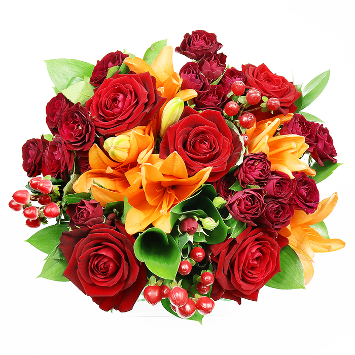 This overhead photograph isolates a luxurious, circular bouquet on a pristine white field, revealing a dense tapestry of warm reds, bright orange, and fresh greens composed with careful floral craft. Prominent are several large, deep red roses, each petal velvety and softly curled back to reveal intricate centres that speak of classic romance and depth. Bright orange Asiatic lilies punctuate the composition with dramatic trumpet forms and visible stamens; some lilies are fully open, presenting sculptural petals, while others sit in elongated buds that promise further bloom. Interspersed throughout the design are clusters of dark burgundy spray roses, their miniature, tightly formed heads creating layered texture and a deeper, wine-toned counterpoint to the primary roses. Small clusters of glossy, round hypericum berries in scarlet add lively punctuation and a smooth, reflective texture that contrasts with the matte softness of the petals. Broad, verdant sprigs of ruscus or salal peek between flowers, their glossy leaves providing structure, movement, and a cooling green backdrop to the warm palette. The photographer's soft, even illumination highlights the interplay of textures - velvet petals, satiny lily throats, and glossy berries - without casting hard shadows, allowing each stem to read clearly from above. The arrangement evokes feelings of celebration, intimate romance, and seasonal warmth, making it suitable for anniversaries, autumn gatherings, or an expressive gift. As a local florist might note while arranging at a bench by the canal near Batchworth Locks, the bouquet balances bold colour with tactile variety to create an image that is both visually sumptuous and quietly eloquent.